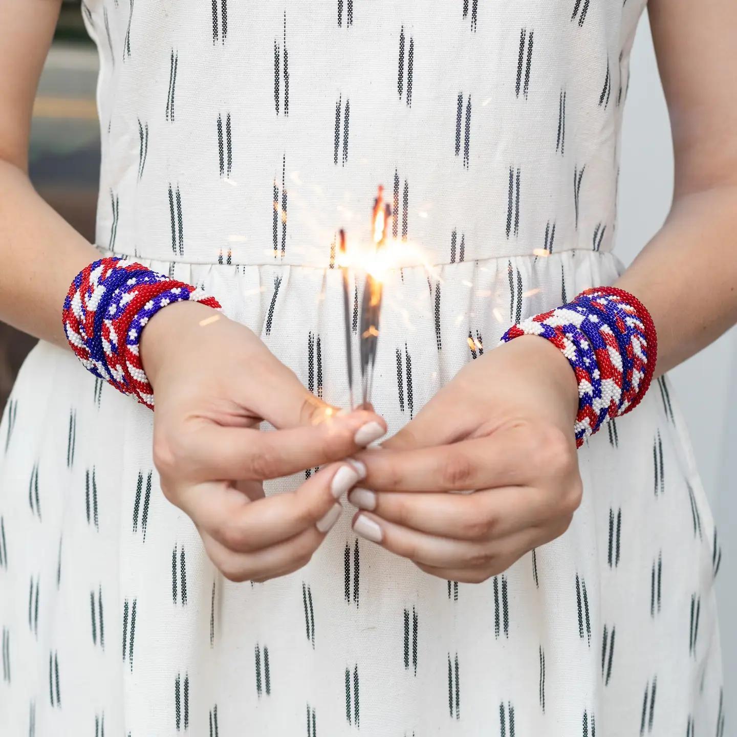 Woman wearing various red white and blue beaded bracelets. 