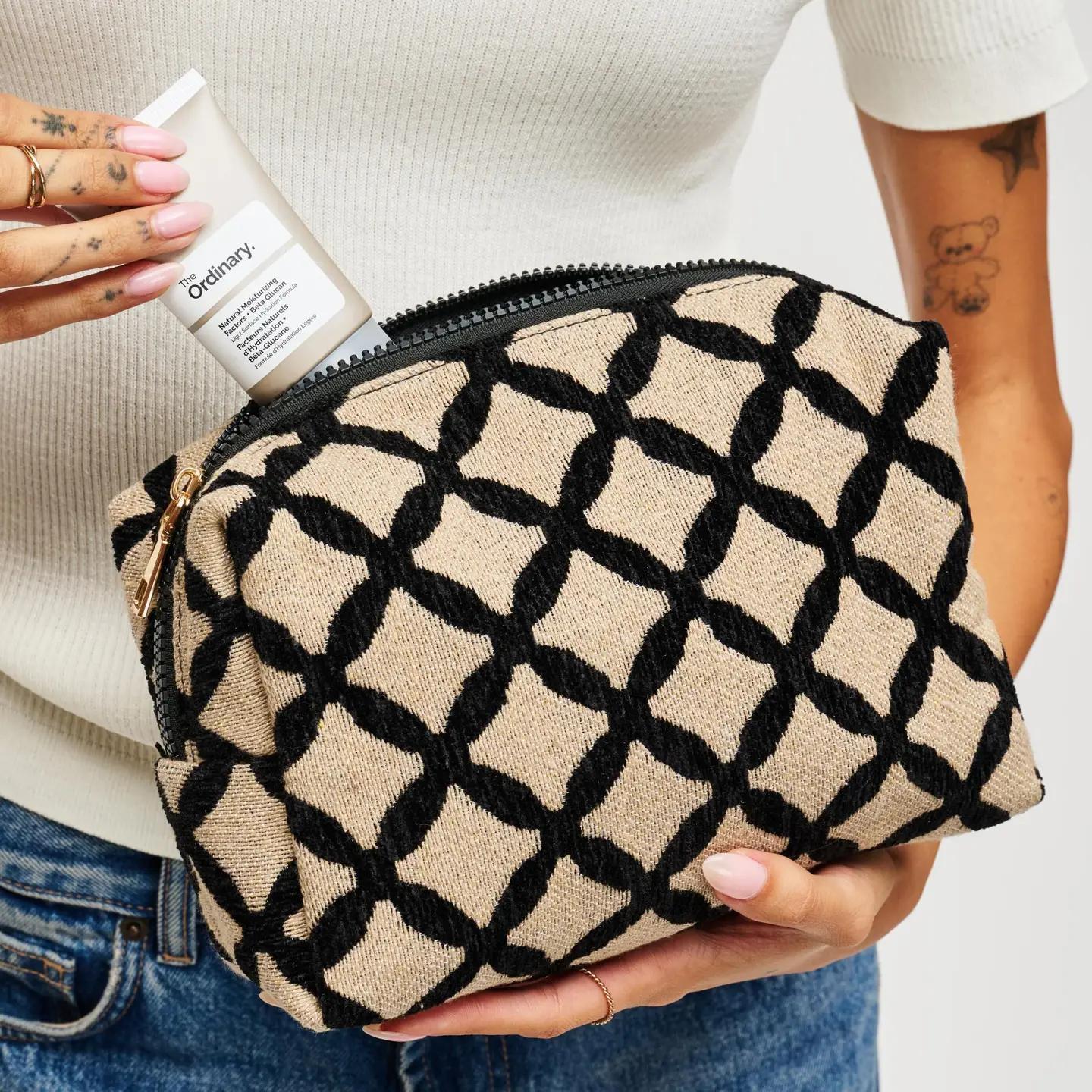 Black and tan makeup pouch with hand putting lotion into pouch. 