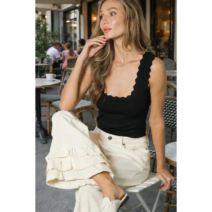 Woman sitting down wearing black tank top and white jeans. 