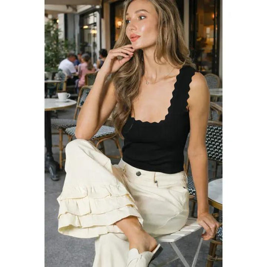 Woman sitting down wearing black tank top and white jeans. 